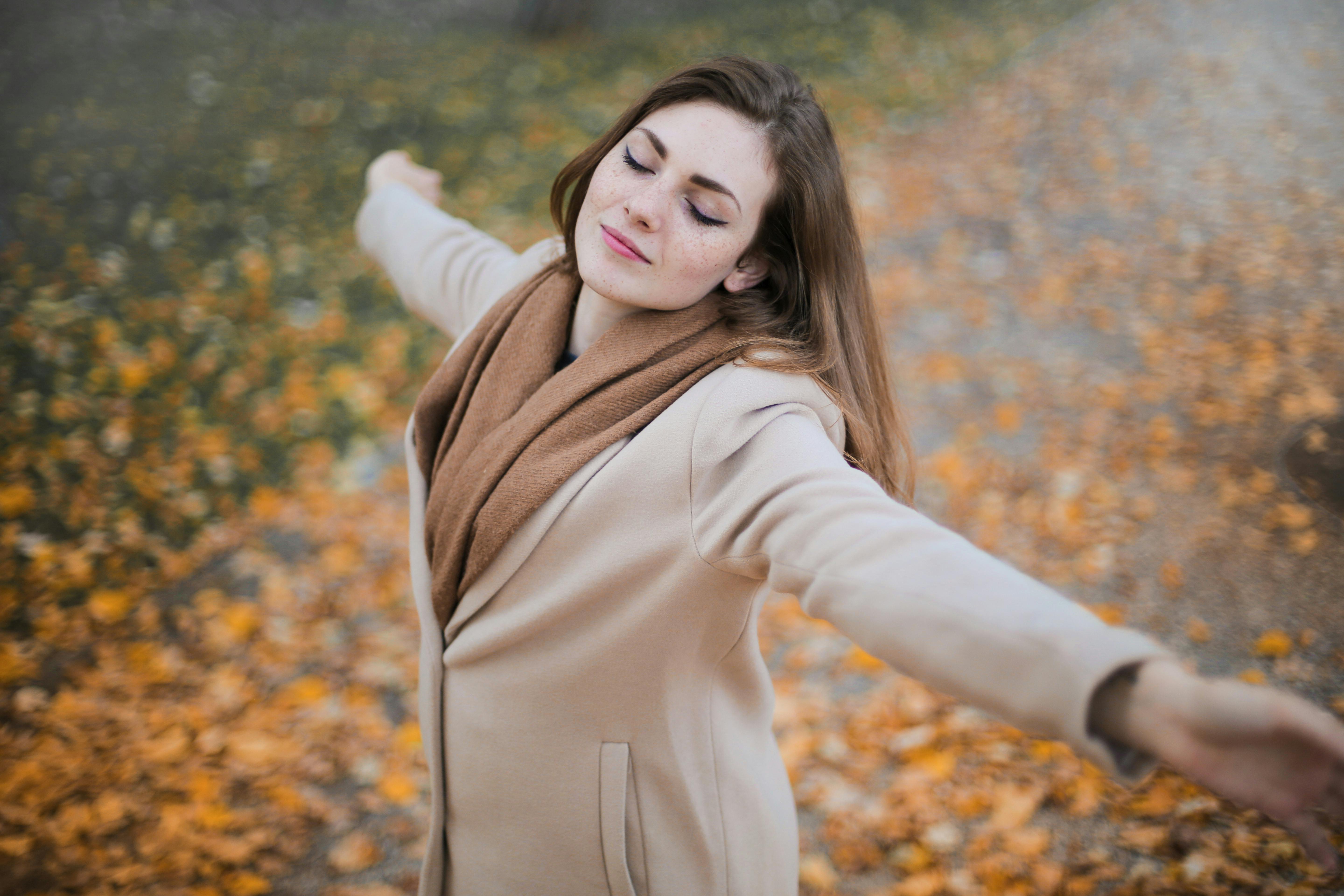 woman in beige long sleeve coat standing on brown leaves