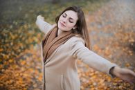 一个女人闭着眼睛，在落叶中拥抱秋天