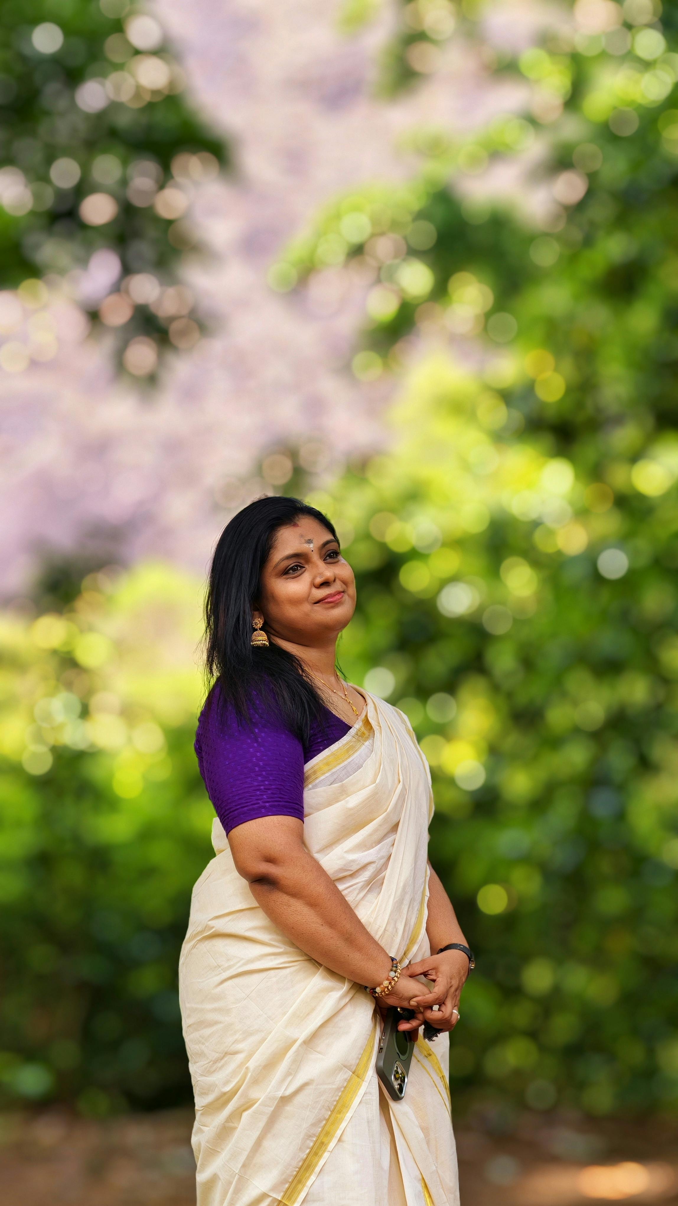 A serene outdoor portrait of a South Indian woman in traditional attire with natural scenery.