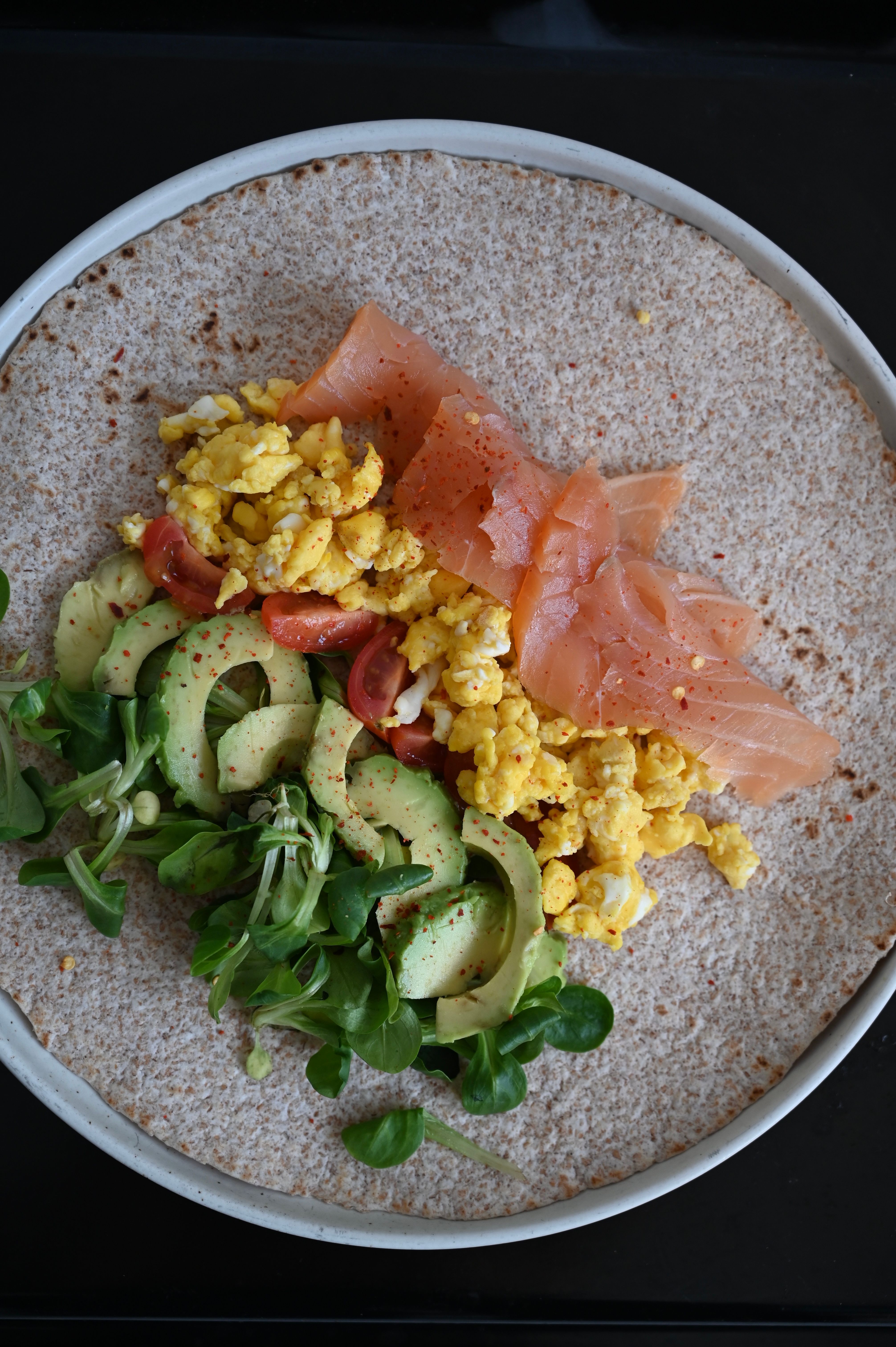 A nutritious wrap featuring smoked salmon, scrambled eggs, and avocado atop a whole wheat tortilla.
