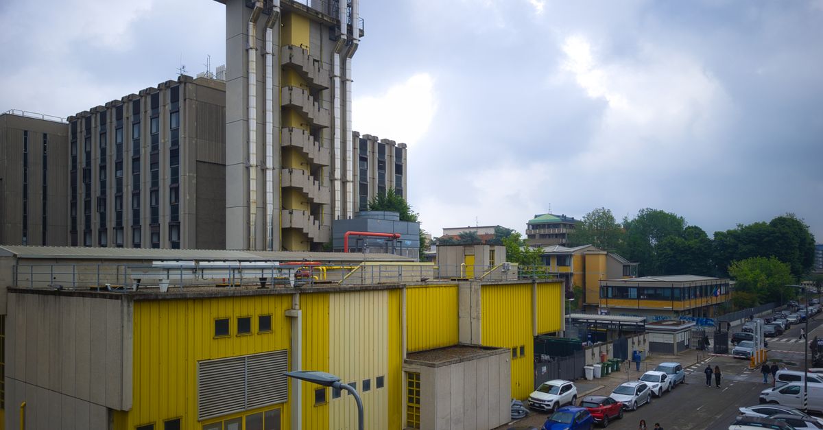 Yellow industrial building next to a parking area in Milan, with cloudy skies overhead.