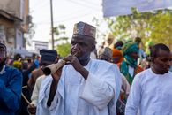 Man playing a traditional horn at a vibrant cultural festival outdoors.