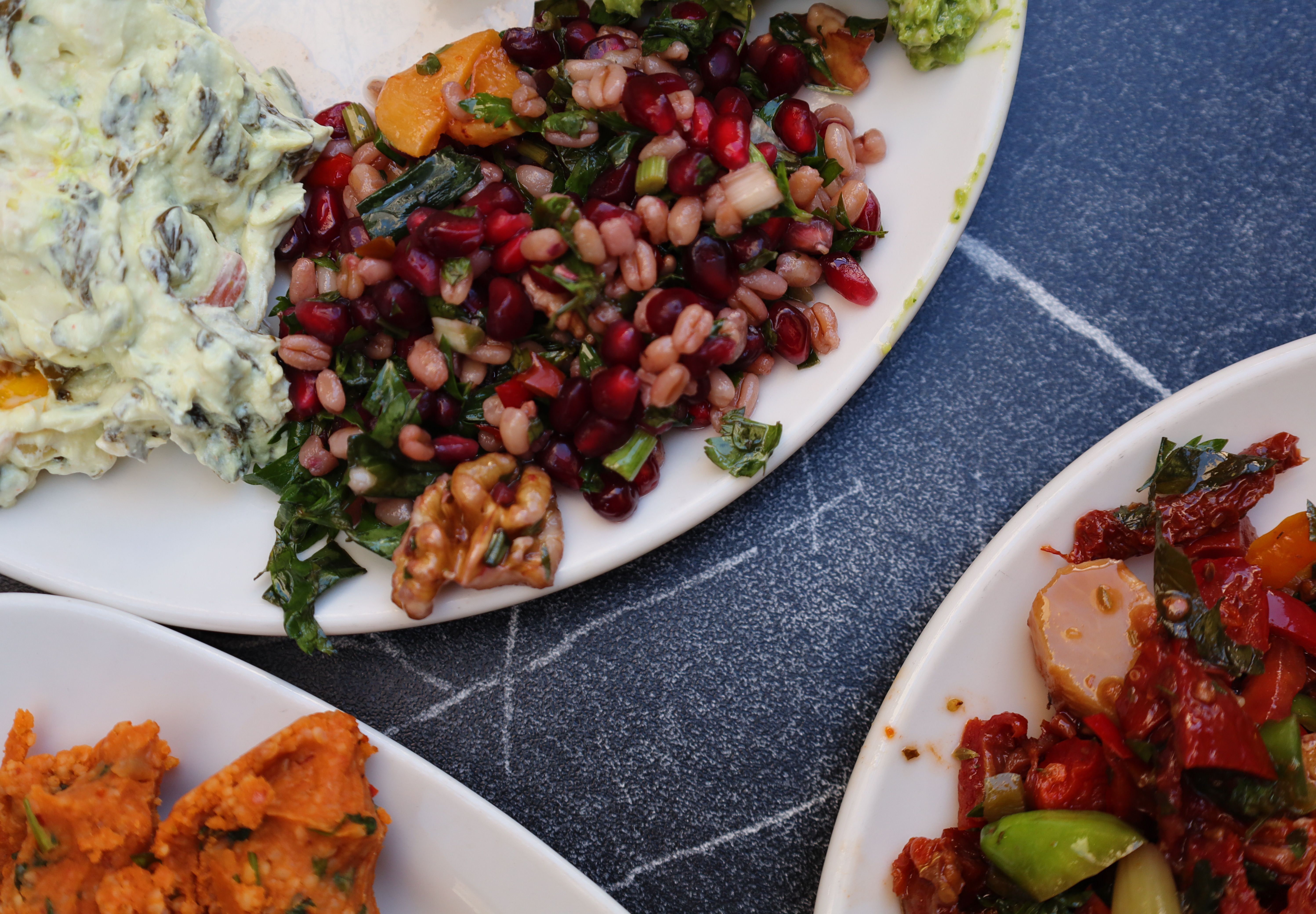 Assorted vegetarian dishes including pomegranate salad and creamy dips on stone surface.