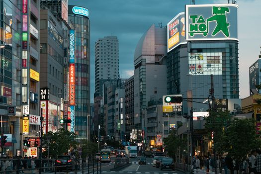 Evening view of a bustling urban street in Tokyo, showcasing vibrant city lights and bustling activity.