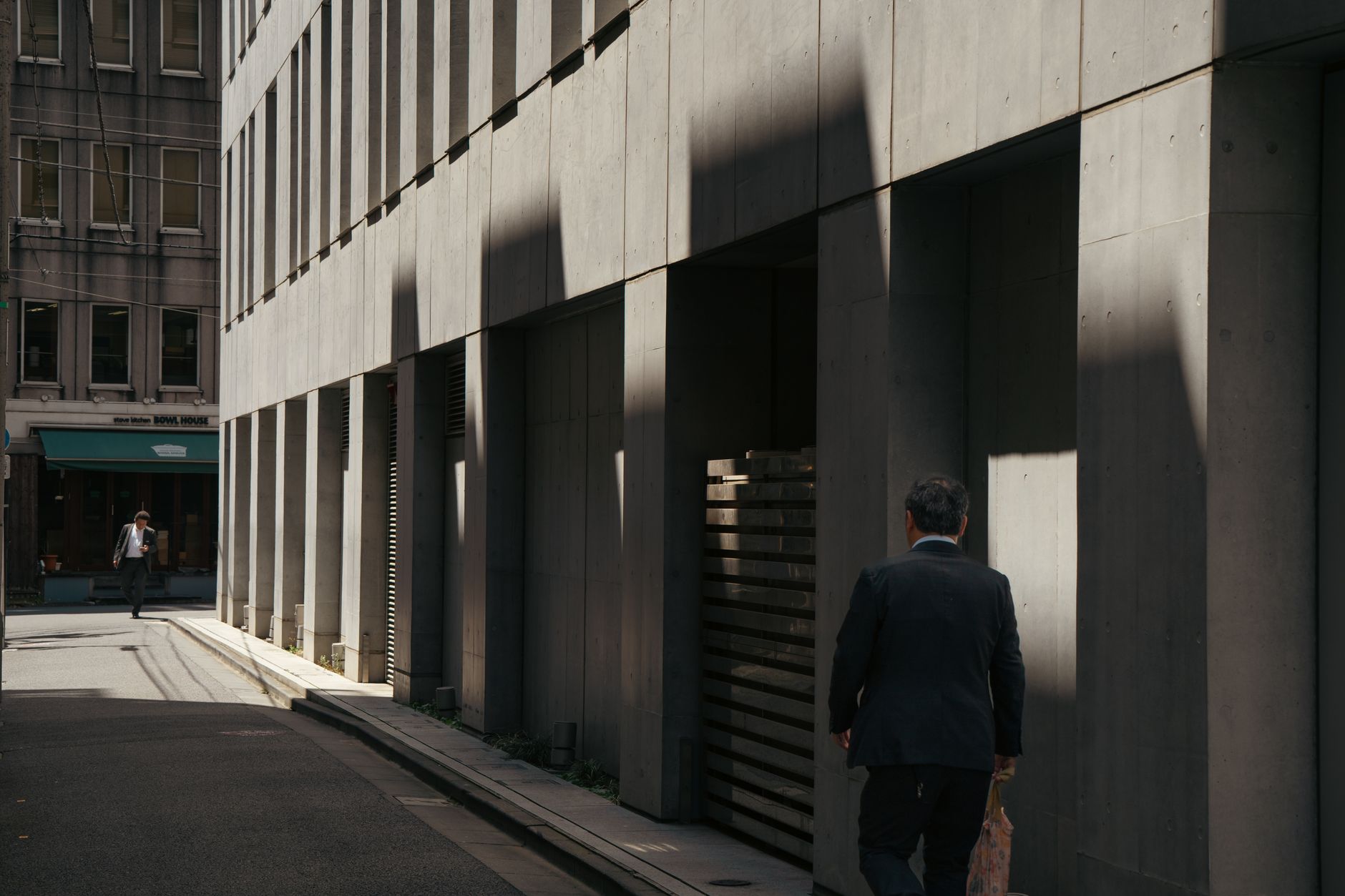 A businessman walks in a sunlit urban alleyway, capturing a mix of light and shadows in a cityscape.