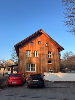 Charming wooden house with cars parked in front, bathed in sunrise light.