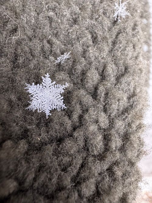 Free Detailed view of delicate snowflakes settled on a warm knitted textile, capturing winter's beauty. Stock Photo