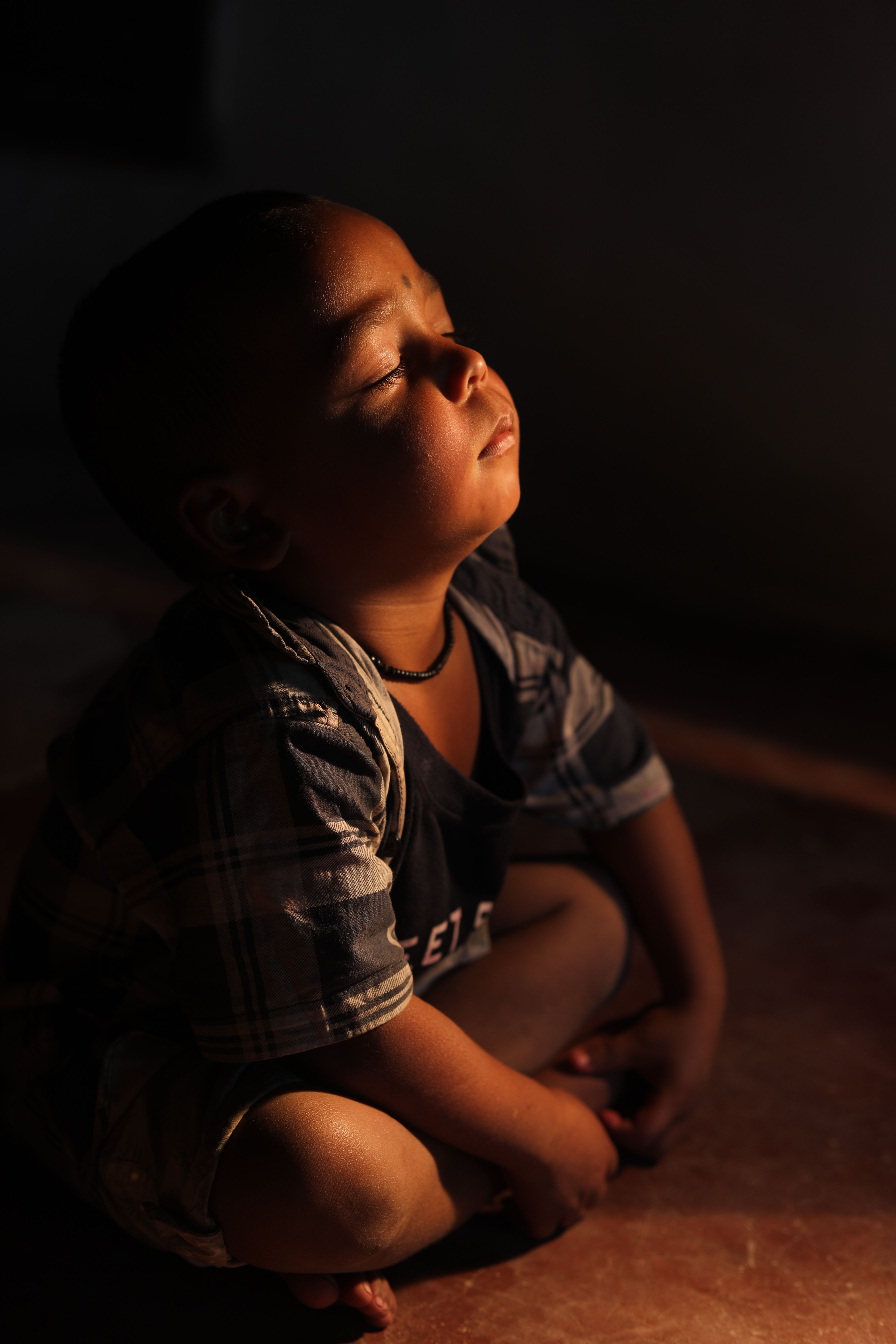A young child peacefully meditates, basking in warm, natural light, showcasing tranquility and mindfulness.