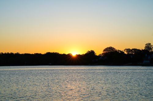 Free A tranquil sunset over a lake with silhouetted trees, creating a peaceful scene. Stock Photo