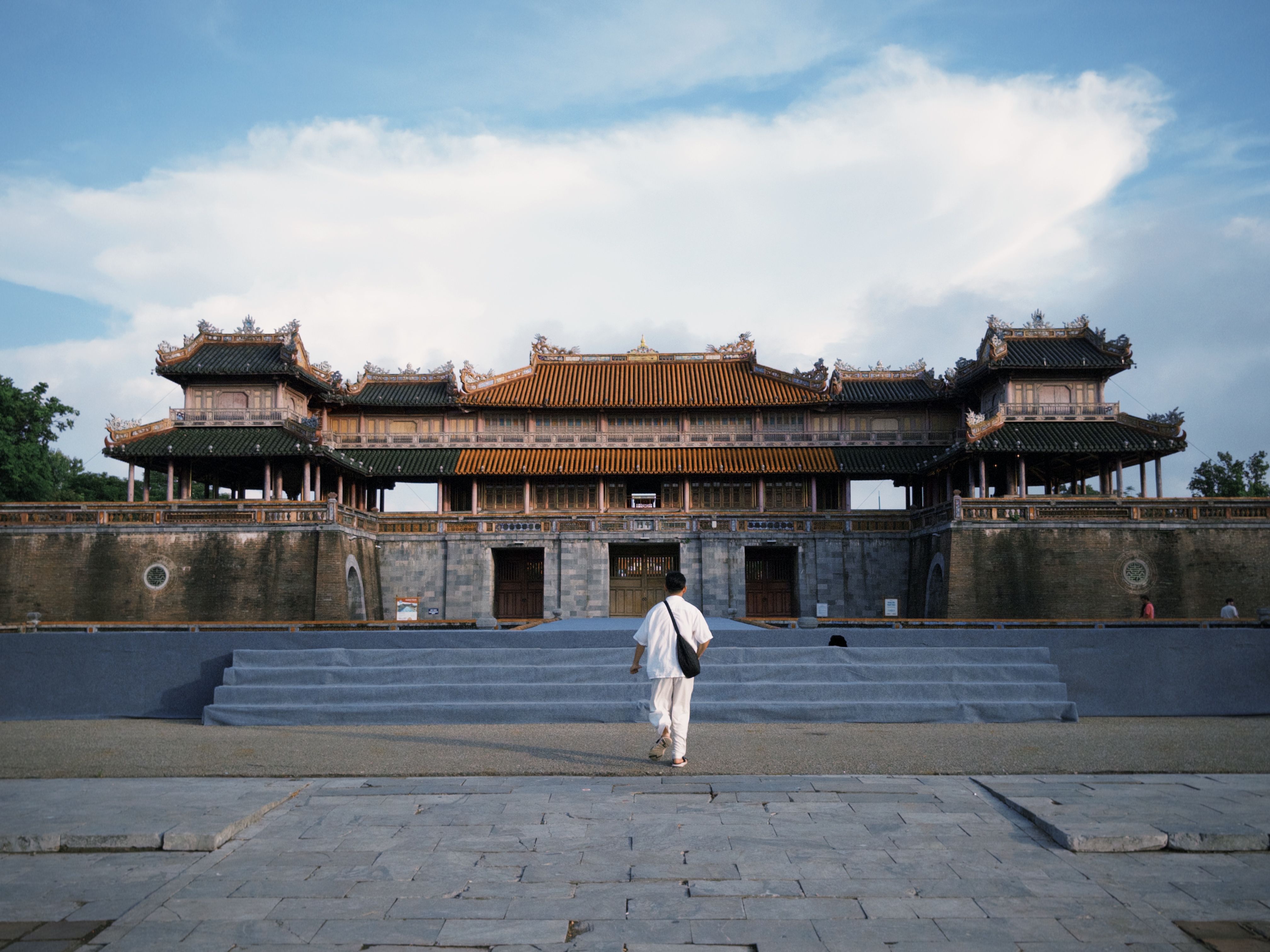 A tourist in white walks towards the historic Imperial City gate in Hue, Vietnam.