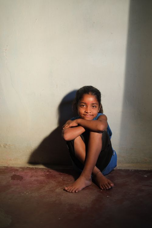 Free A young girl sits on a shaded floor, smiling warmly in a sunlit room. Stock Photo