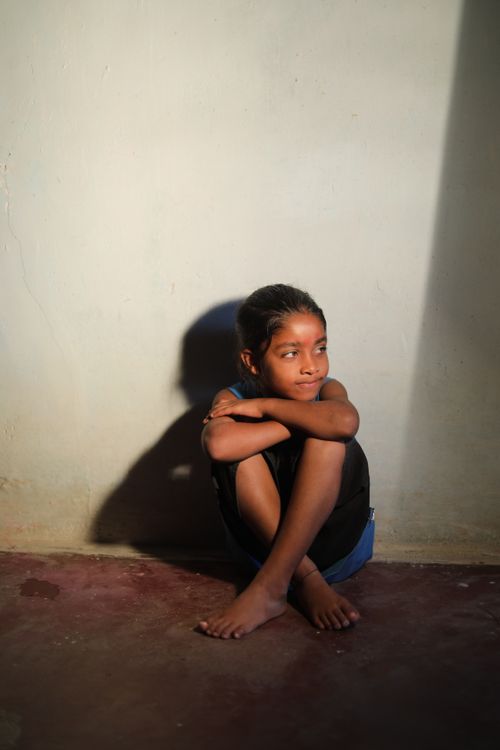 Free A South Asian child sits in soft sunlight against a wall, creating a contemplative mood. Stock Photo