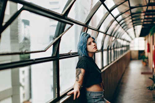 Selective Focus Photo of Woman with Blue Hair in Black Shirt and Blue Denim Shorts Standing on Empty Corridor