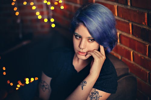 Photo of Tattooed Woman with Blue Hair in Black T-shirt Thinking