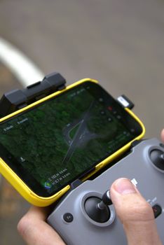 Close-up of hands operating a drone controller with a smartphone showing a forest aerial view.