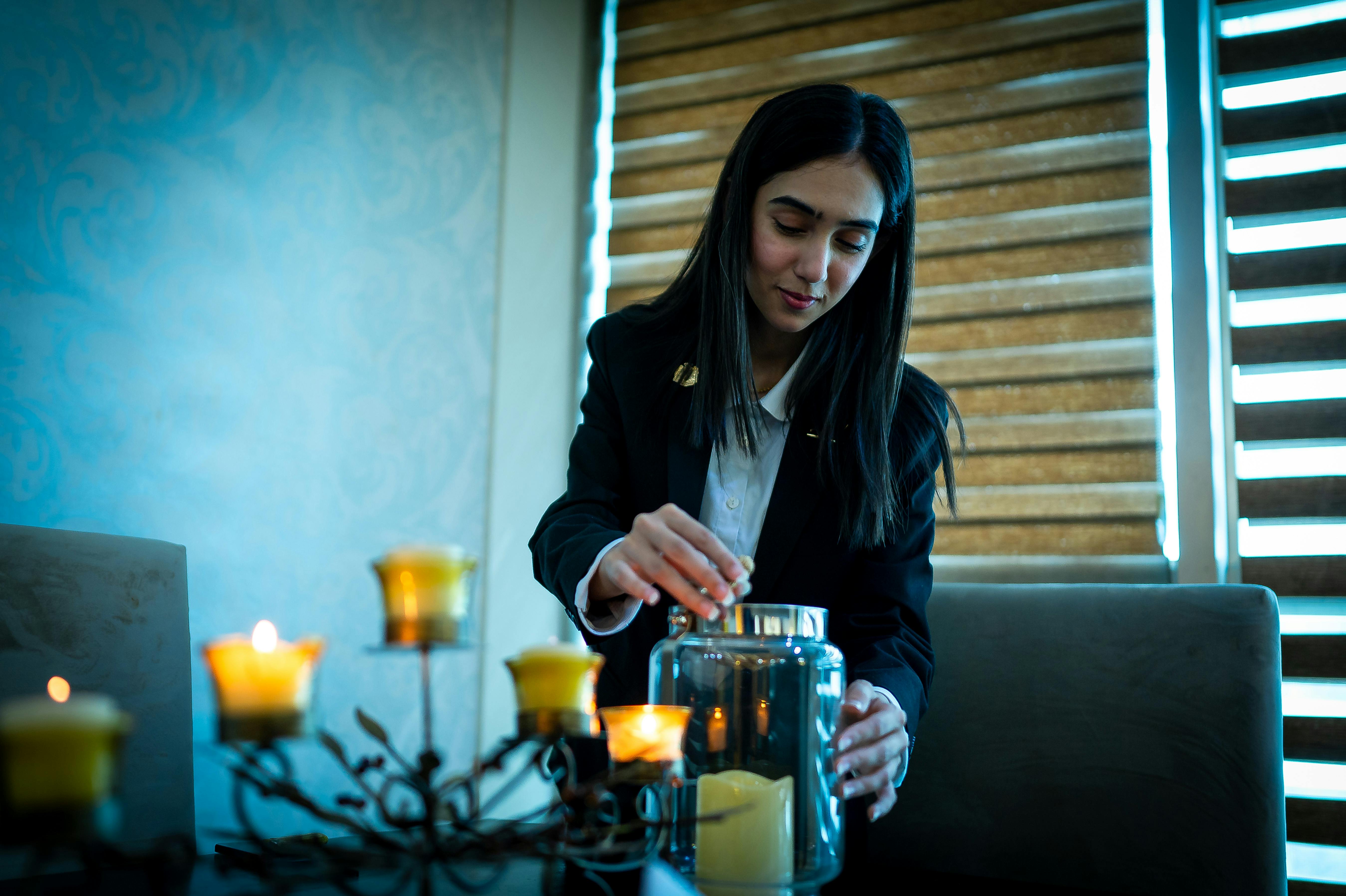 A woman adjusts candles indoors, creating a warm and inviting atmosphere with soft lighting and decor.