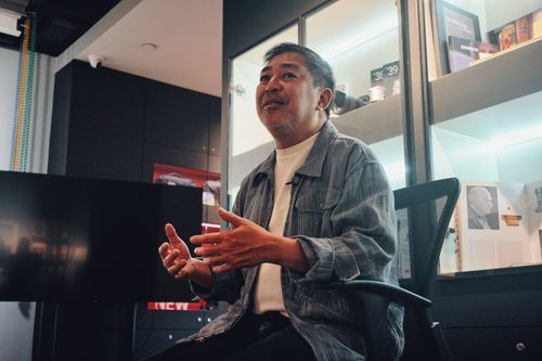 Free A man speaks animatedly during an office discussion, seated in a modern workspace with display shelves. Stock Photo
