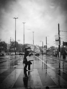 A person with an umbrella crossing a wet street on a rainy day in black and white.