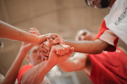 From below of crop multiethnic team of professional basketball players gathering and putting hands together while standing on playground before game