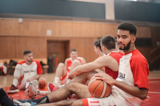 Male basketball players resting on an indoor court, holding basketballs.