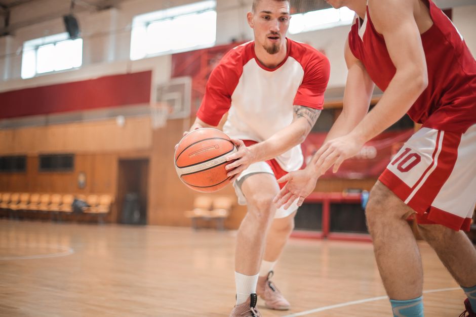 Two male basketball players practicing dribbling indoors. Intense focus and skill displayed.