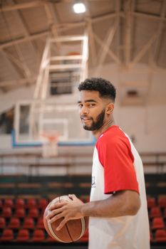 Focused young male basketball player holding a ball in an indoor gym.