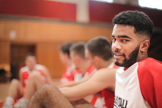 A group of young basketball players sitting casually indoors, wearing red and white jerseys.