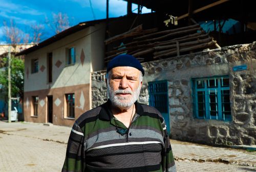 Free Senior man with a beard in outdoor village street, standing in front of a rustic building. Stock Photo