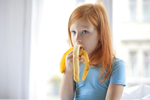 Free Girl in Blue Crew Neck T-shirt Eating Yellow Banana Stock Photo