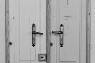 A minimalist black and white photograph of vintage double doors, showcasing ornate metal handles.
