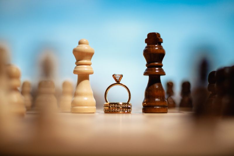 Creative shot of gold wedding rings between chess pieces outdoors against a clear blue sky.