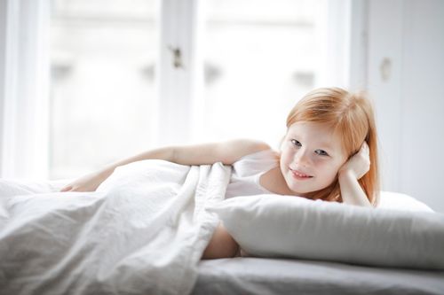 Free A cheerful young girl with red hair lying on a bed in a bright, cozy bedroom. Stock Photo