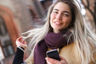 一位年轻女子戴着围巾，在户外拿着智能手机微笑