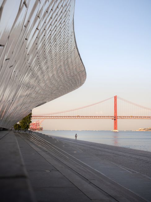 Elegant architectural curves with Lisbon's iconic 25 de Abril Bridge at sunrise.
