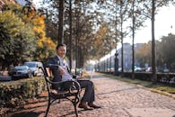 秋日阳光下，一位面带微笑的商人坐在公园的长凳上，用笔记本电脑在户外工作