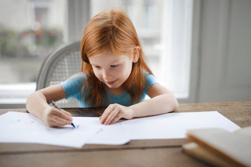 Free Diligent small girl drawing on paper in light living room at home Stock Photo
