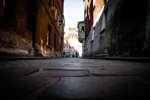 Sunlit alleyway in Warsaw's historic Old Town, showcasing architectural charm and European street life.