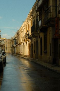 A picturesque street in Malta capturing beautiful light reflections on wet pavement after rain.