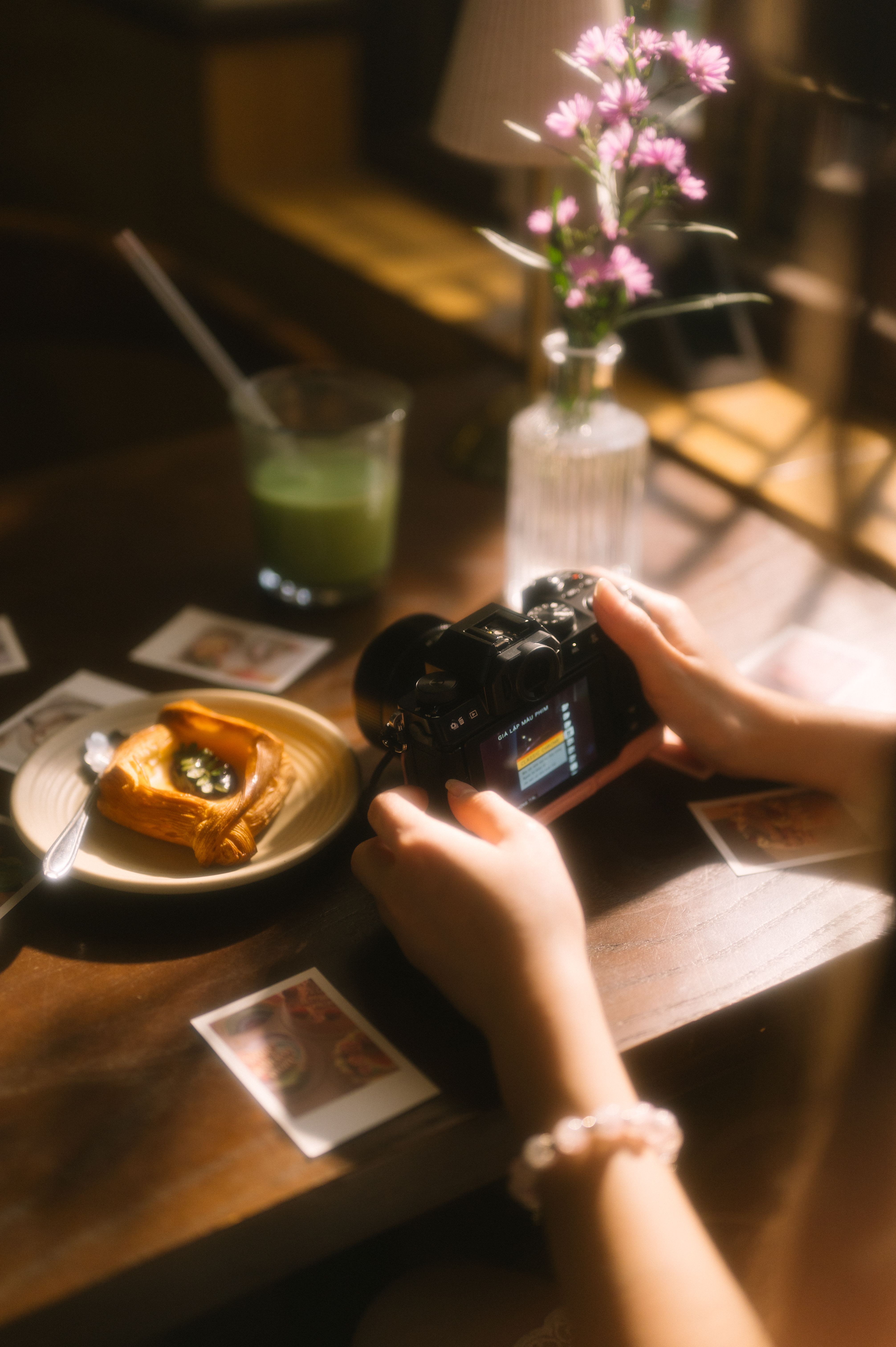 A person photographing a pastry and drink on a sunlit table, evoking vintage and cozy feelings.