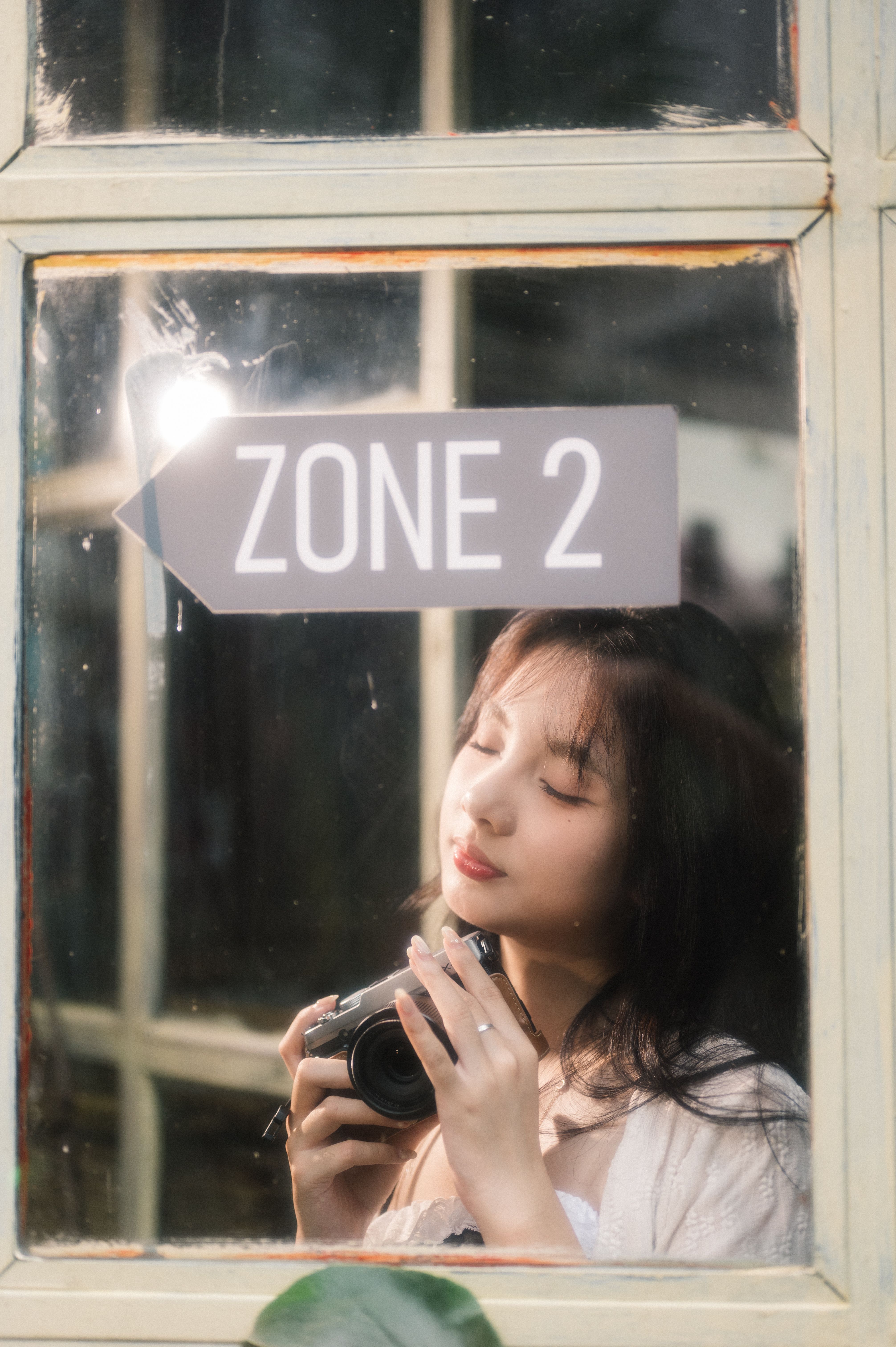 A serene portrait of a woman holding a camera, reflected in a window marked 'Zone 2' in Lạng Sơn, Việt Nam.