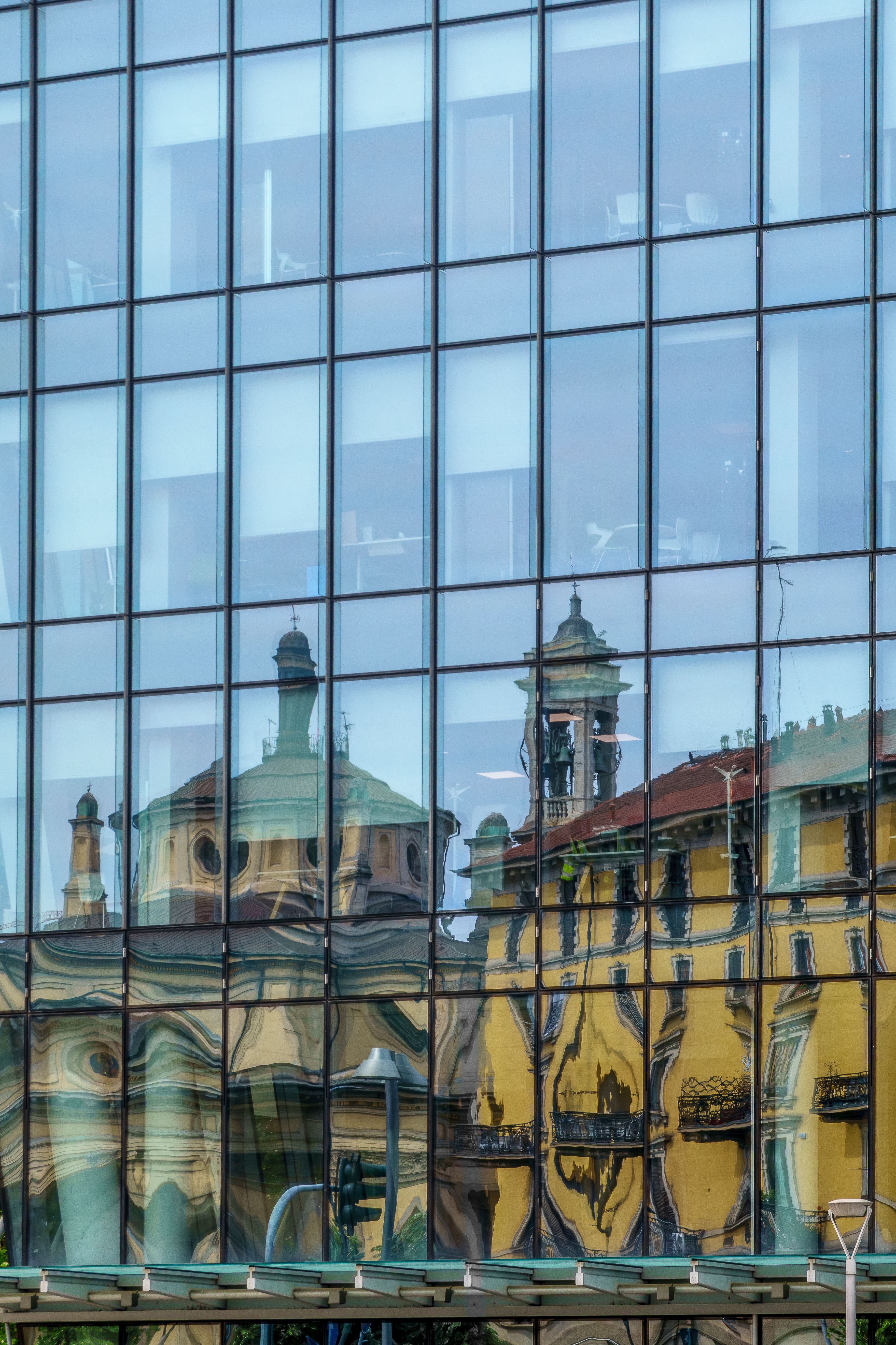 Distorted historical architecture in glass facade of modern building.