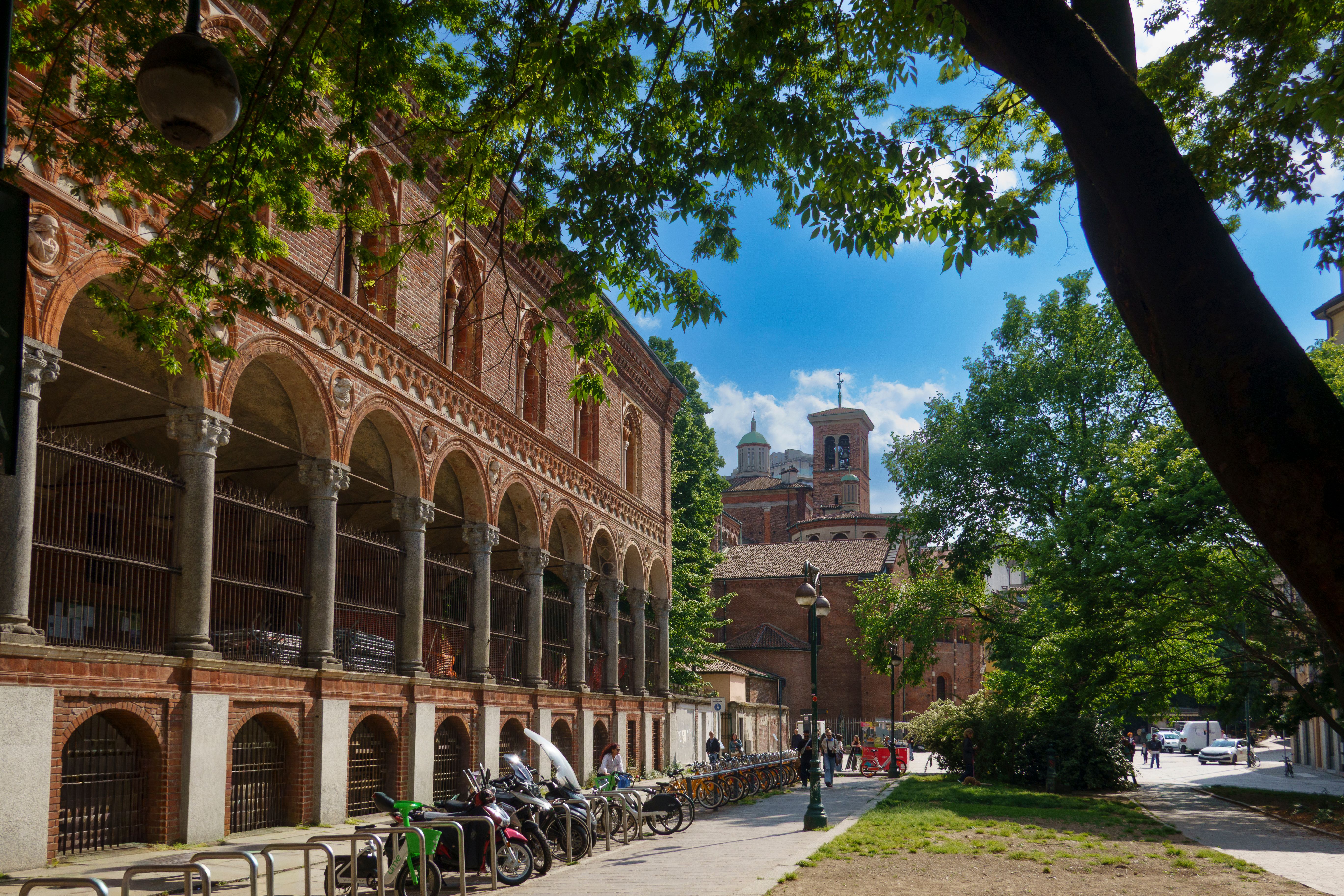 A scenic view of a historic red brick building in Milan, Italy, under a clear blue sky.