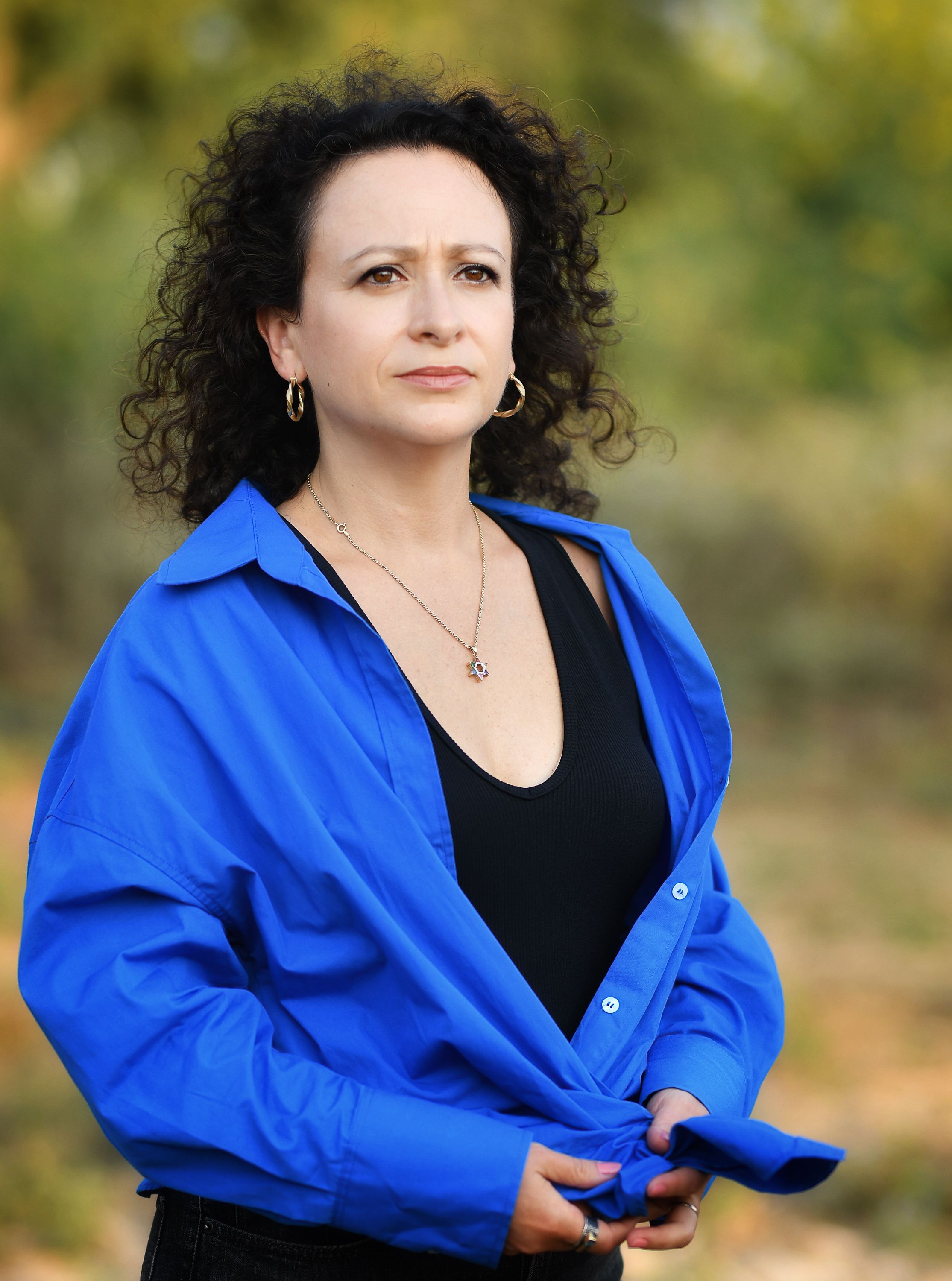 Confident woman in a blue shirt poses naturally outdoors, with a calm demeanor.
