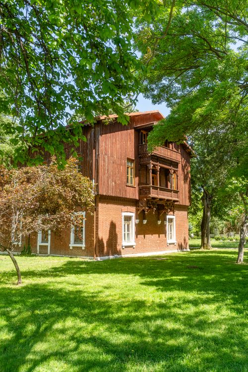 Free A rustic brick and wood house surrounded by vibrant green trees and grass in summer. Stock Photo