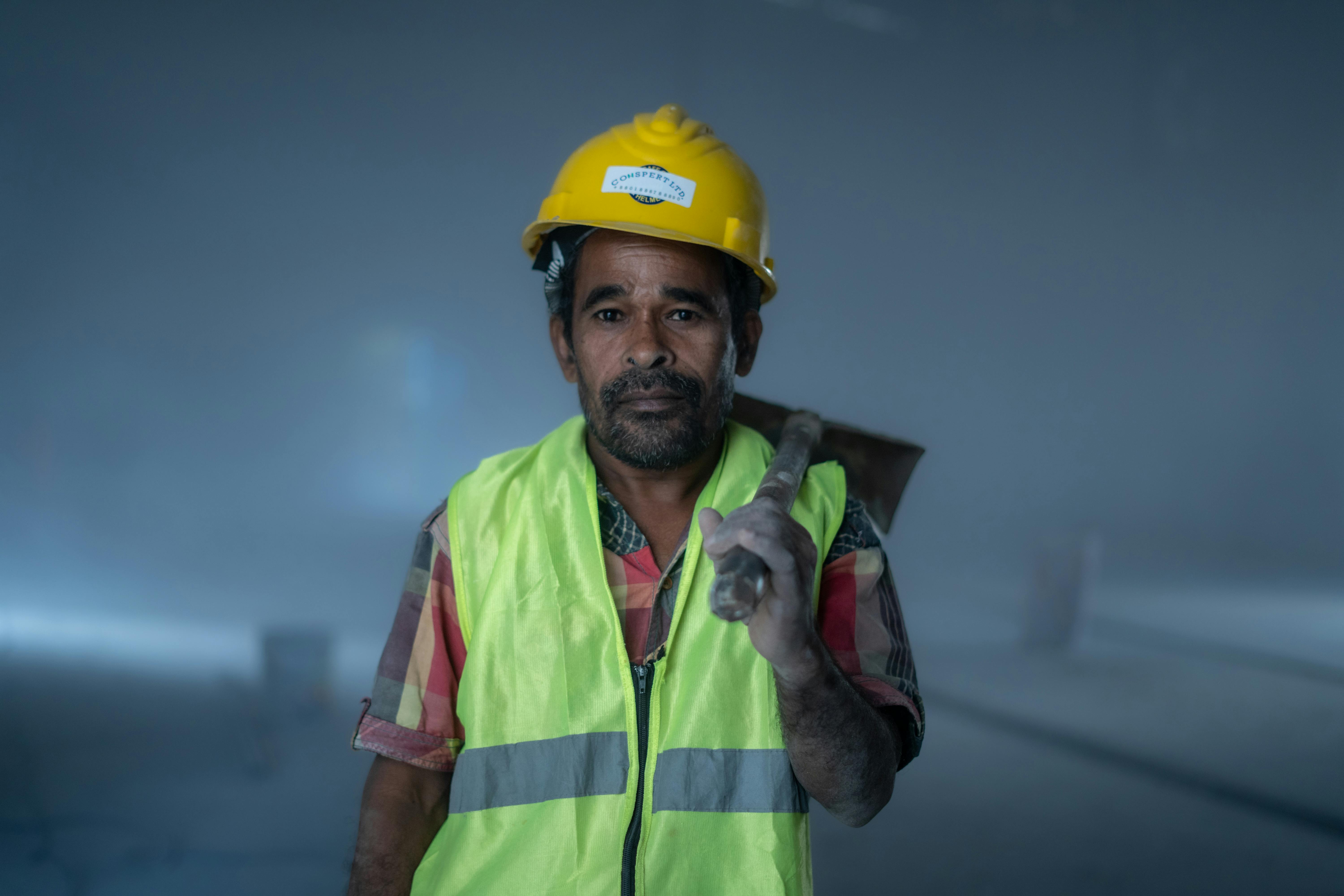 Portrait d'un ouvrier du bâtiment en tenue de sécurité sur un chantier industriel, symbolisant le labeur et la détermination.