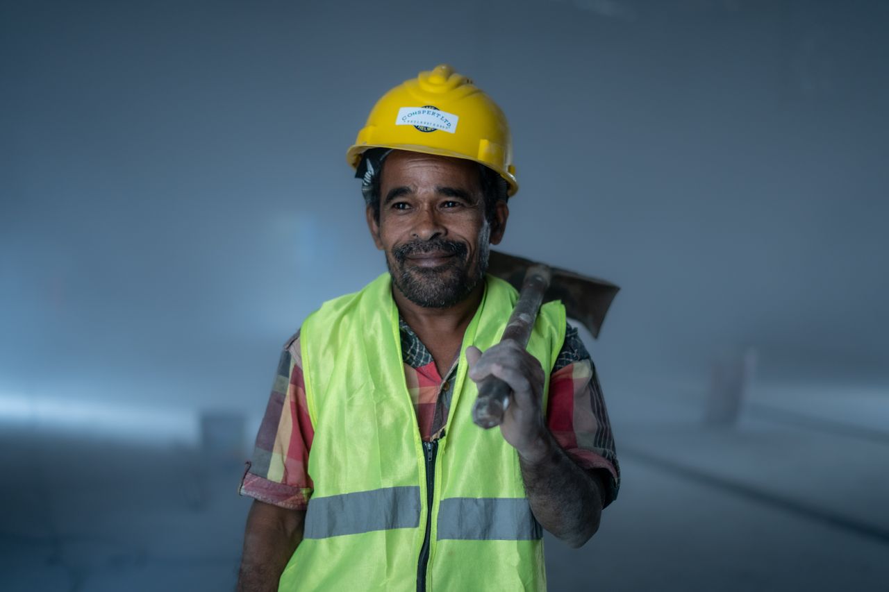 smiling construction worker in safety gear holding a tool indoors prof