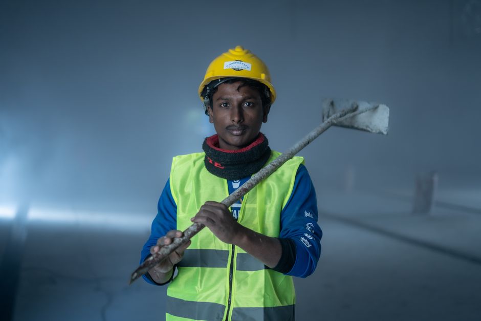 Portrait of a construction worker in safety gear holding a tool in an industrial setting with misty atmosphere.