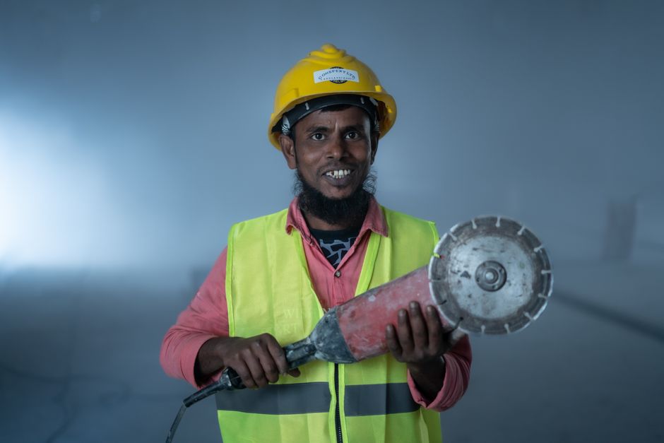Construction worker holding a power tool, wearing safety gear on site.