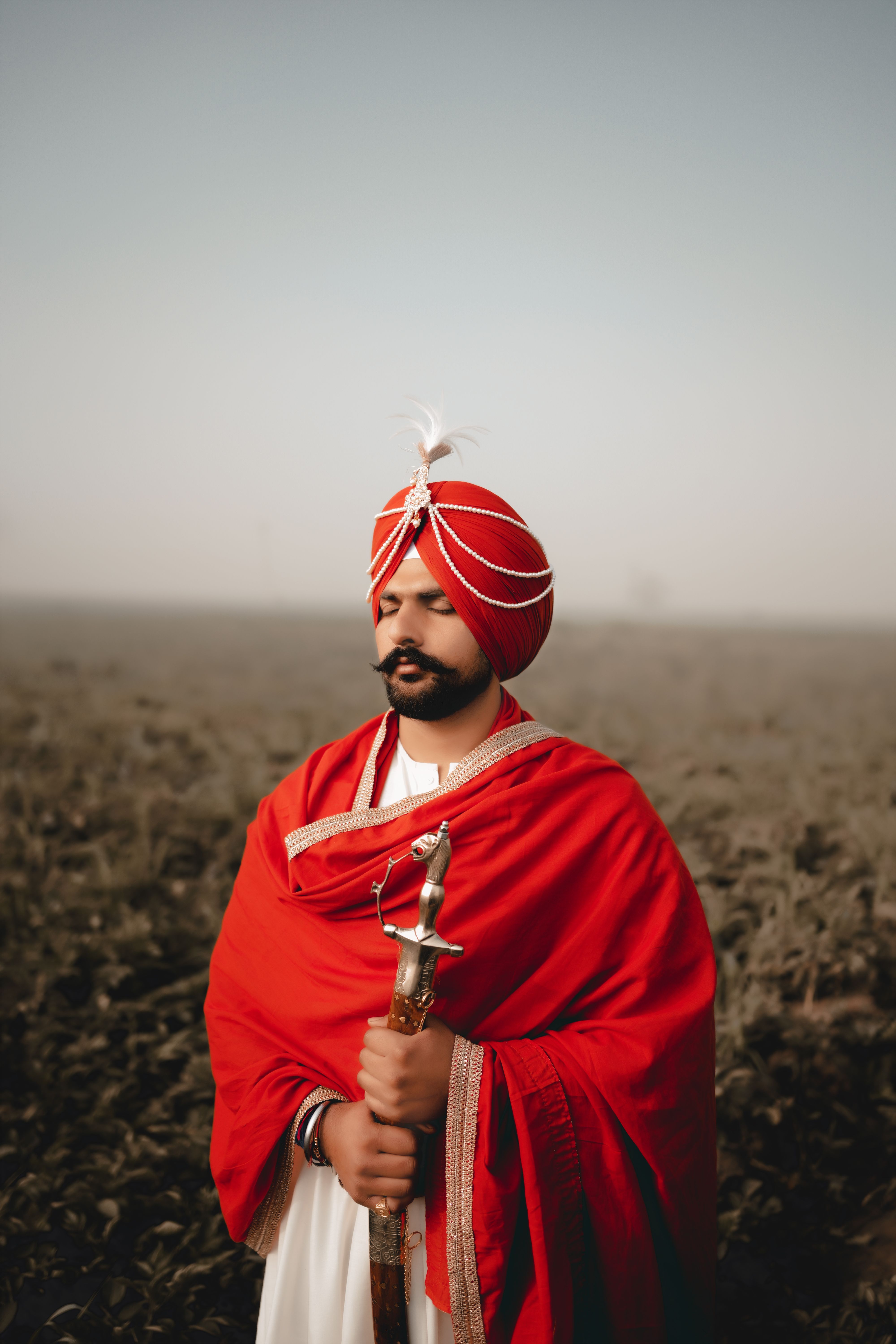 Sikh groom in traditional red attire standing outdoors, holding a sword in Amritsar, Punjab, India.