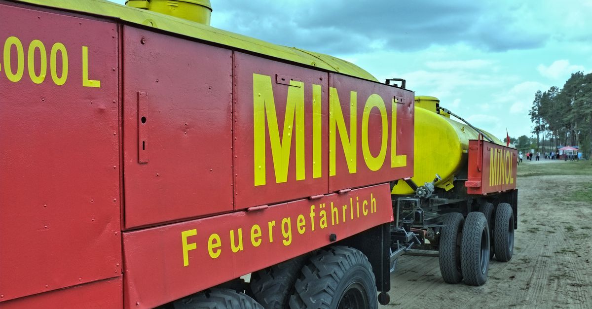 A bright red and yellow MINOL tanker truck with labeled compartments parked outdoors under a cloudy sky.